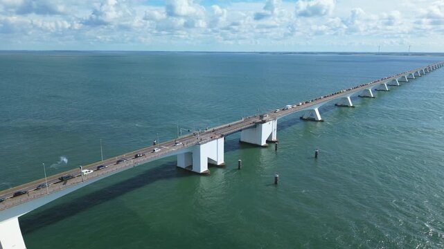 Cars driving across Zeelandbrug, a long bridge over the Oosterschelde estuary in the Netherlands under a cloudy sky