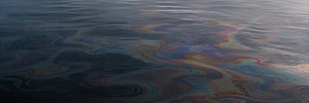 Rainbow oil slick floating on dark water with copy space, website banner, pollution, ecology