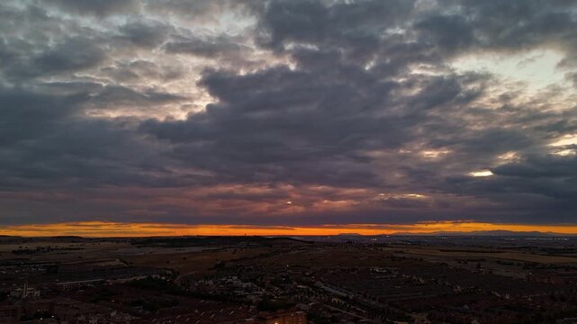 Hyperlapse aerial drone footage of dusk and blue hour over Valdemoro in southern Madrid, Spain, with clouds moving over an orange horizon and town lights below