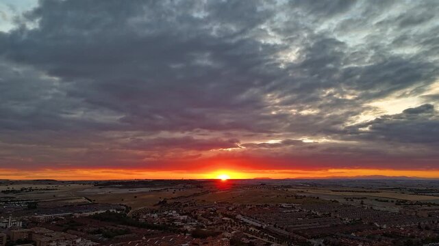 Hyperlapse aerial drone footage of a sunset over Valdemoro in southern Madrid, Spain, with clouds moving over flat plains and town rooftops below