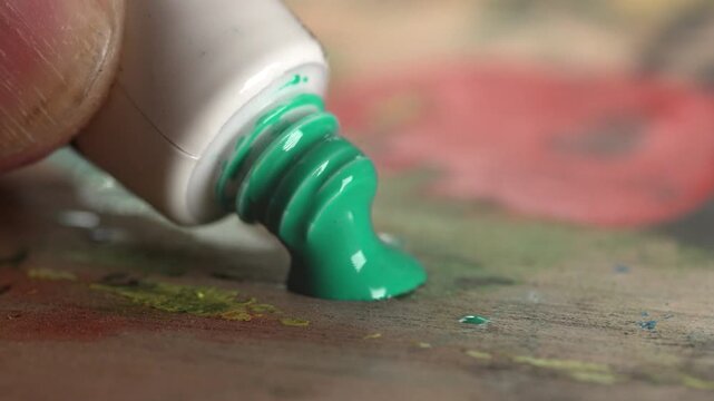 Extreme close-up of hand squeezing out vibrant green paint from a tube onto a palette.