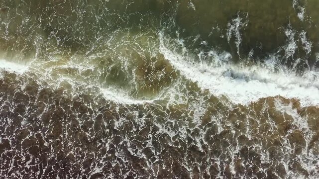 Waves move in and out on the sand at a beach under bright sunlight. The water shows various shades as it flows towards the shore, creating movement and energy.