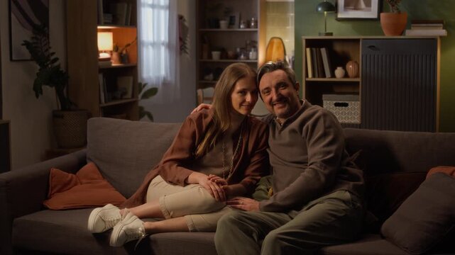 Wide shot of Caucasian middle aged couple sitting on sofa and smiling at camera. Video represents perfect visual for family counseling, real estate, or home insurance campaigns