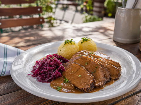  Tafelspitz tradicional servido con salsa, col lombarda estofada y bolas de patata en una terraza de restaurante.