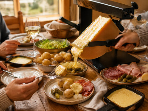  Raclette suiza con queso caliente fundido directamente sobre patatas, acompa&ntilde;ado de embutidos, pepinillos y una comida compartida alrededor de la mesa.