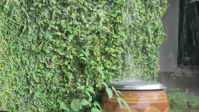 Rainwater pours down onto a traditional Thai clay jar with a dragon pattern during a heavy storm