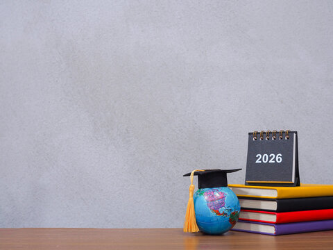 Student creative desktop, Earth globe with graduation hat and 2026 desk calendar on hardcover book. Copy space for text, Back to school, Education concept