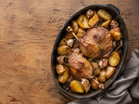 Pato asado con patatas doradas y chalotas, presentado en una fuente para compartir en una comida familiar.