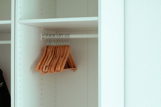 Wooden hangers neatly arranged on a metal rod inside a minimalist white wardrobe with empty shelves and a black garment hanging on the side