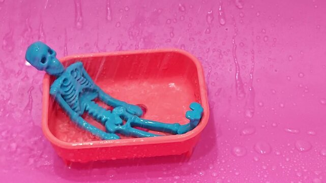 Small blue skeleton relaxes in a red tray while water splashes around
