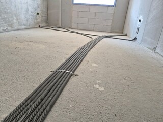 Obraz premium Corrugated plastic electrical pipes laid out and fixed with plastic clamps to the concrete floor grid inside a newly built residential apartment. Underfloor wiring infrastructure and construction phas