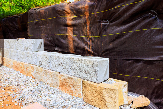 Construction workers are laying stones to build retaining wall at site area is prepared with gravel fabric.