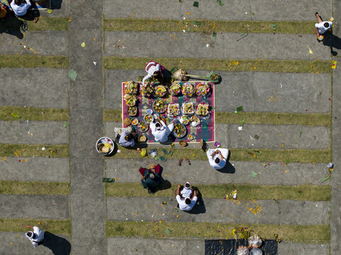 Aerial view of people performing traditional Kuningan Day offerings with colorful baskets and flowers on a patterned ground in Kecamatan Kintamani, Bali, Indonesia.
