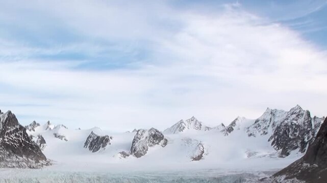 A sweeping view of a pristine Arctic glacier, flanked by rugged, snow-covered mountains, captures the sublime stillness of this remote polar environment on a clear day.