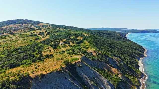 Green hills rolling down to a coastline. The sea is calm and blue, while the sky is clear and bright. There are no people present in this natural setting.