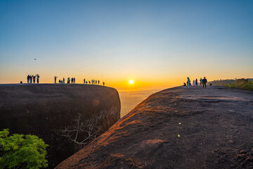 Obraz premium Silhouetted travelers gather on the massive rock formation of Three Whale Rock, watching the first light of day spread across the misty countryside of northeastern Thailand.