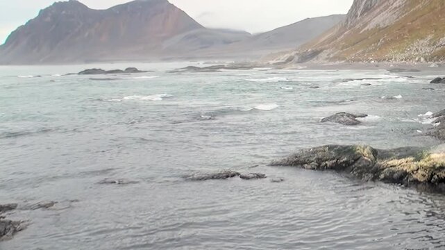 The Arctic waters of Svalbard, Norway, ebb and flow against the dark, ancient rocks.