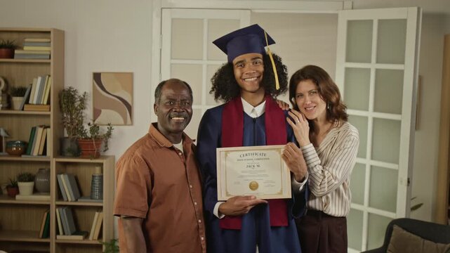 Portrait of African American teenager in graduation gown holding certificate with Caucasian middle aged mother and African American middle aged father. Clip is ideal for education marketing
