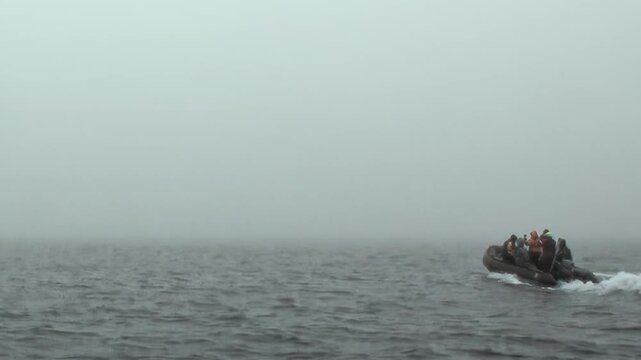 Adventurers journey aboard a small, swift vessel across the vast, choppy waters of the Arctic Ocean. A thick mist hangs over the waves under a somber, cloudy sky, creating a wild seascape.