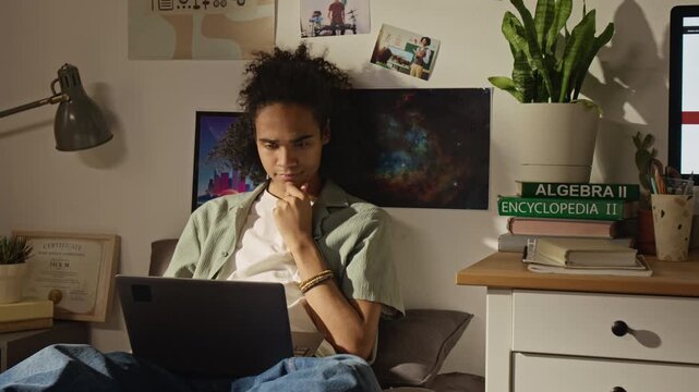 Medium shot of African American teenager studying with laptop in bedroom, feeling curious and rubbing chin. Ideal for online education, e-learning platforms, student lifestyle marketing campaigns