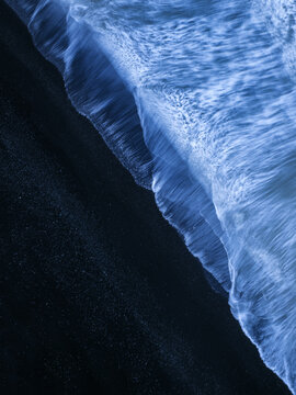 Aerial view of the dramatic black sand beach with white sea foam washing over the dark volcanic shore, Vik, Myrdalshreppur, Iceland.