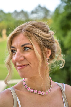 ​Elegant mid-adult blonde woman with pink crystal jewelry looking away, outdoor beauty portrait