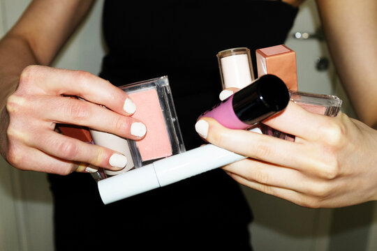 Hands holding bunch of makeup beauty products blushes, mascaras, lip 