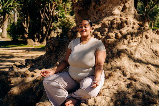 A woman meditates sitting on the root of a tree