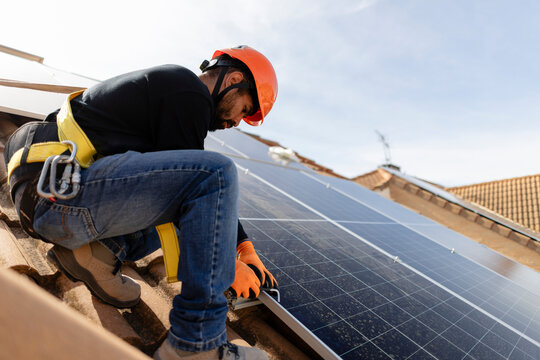 Worker installing solar panels on house rooftop