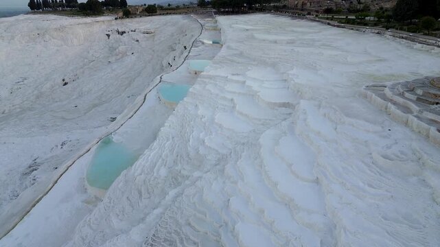 Dawn's soft light embraces the vast white travertine terraces of Pamukkale, Turkey. Faint purple and gold hues paint the thermal pools below as the morning begins. Mountains stand dark in the backgrou