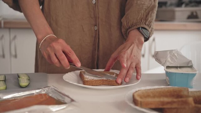A person spreads jam on a piece of toast in a kitchen. They use a knife and a plate while getting ready for breakfast. The kitchen looks bright and organized.