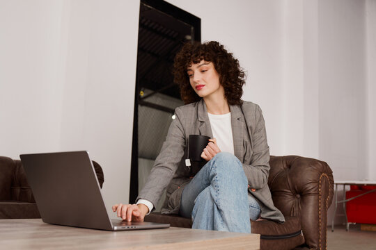 Woman Working on Laptop While Holding a Cup in a Cozy Space
