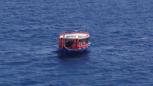 Aerial view of a Maldivian dhoni off Dhigurah island, Maldives. The boat bobs and drifts, ladders and roof storage visible, midday sun highlights ripples.