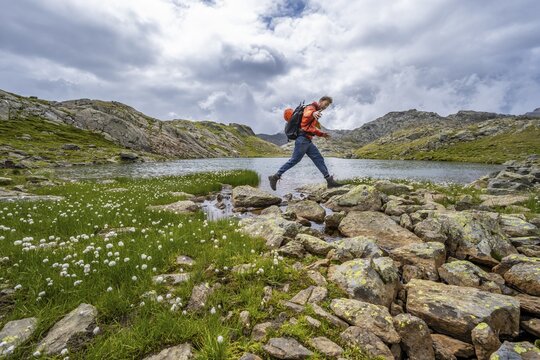 Mountaineer jumping from stone to stone, at a mountain lake in high mountain landscape at the Obere Senner Egete, Seven Lakes Hike, Stubai Alps, near Ridnaun, South Tyrol, Italy