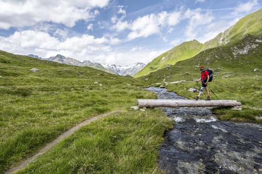 Mountaineer crossing a stream on a tree trunk, mountain landscape with mountain stream, Las&ouml;rling Group, Hohe Tauern National Park, East Tyrol, Austria