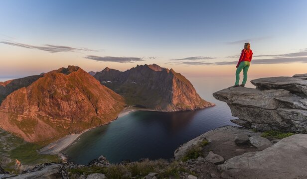 Evening atmosphere, hiker on top of Ryten, sea, Kvalvika beach and mountains, Fredvang, Lofoten, Nordland, Norway