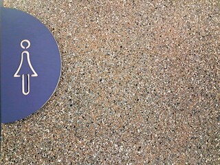 Female restroom sign icon on textured stone wall background, ideal for public facility wayfinding design, commercial washroom signage mockup, and architectural presentations with copy space. © Fiqih