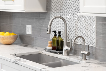 Sink detail shot in a luxury kitchen with white herringbone and grey subway backsplash tiles, white...