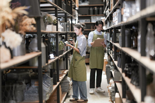 Small business partners reaching for goods on a high shelf using a step ladder in a rustic wooden warehouse. Conveying a warm family business spirit. Business concept.