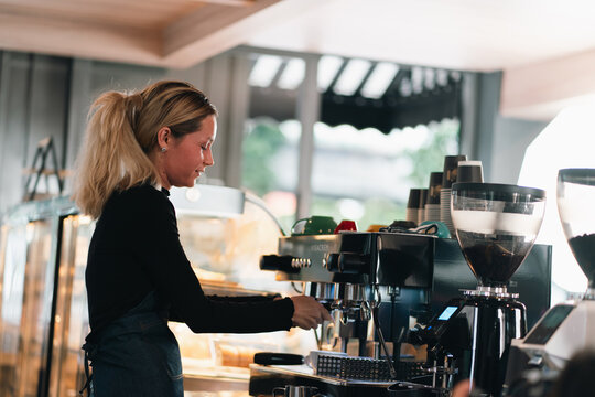Coffee shop barista woman espresso machine cafe counter service beverage preparation work apron blonde hair