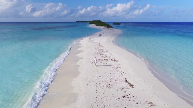 Aerial view of Dhigurah, Maldives, shows a narrow sand spit curving into the Indian Ocean, shallow lagoon left, deeper sea right, lone walker, bright daytime light