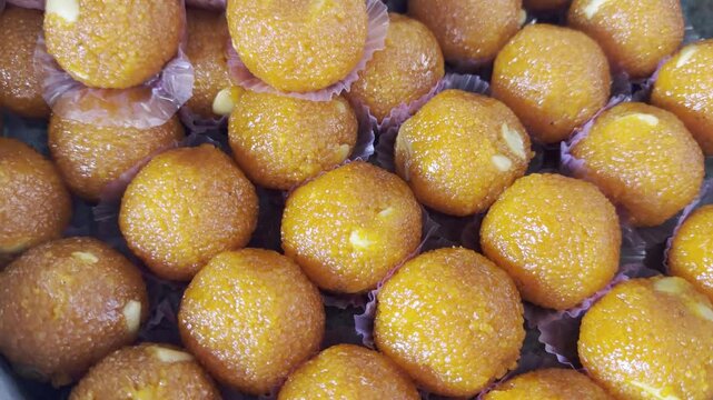 Close-up 4K video of bright orange Indian laddus arranged in a glass display at a sweet shop, showcasing their glossy texture, traditional dessert appeal, and festive food presentation.