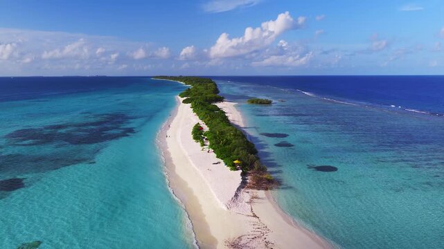 Aerial view of Dhigurah island, Maldives, shows a narrow sandbar, central green ribbon, turquoise lagoon, cobalt ocean, tiny boats, umbrellas, and walkers in bright daylight.