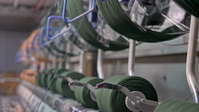 Green yarn bobbins operate on a winding line inside a textile factory. This video frame shows yarn transfer, bobbin winding, industrial machine detail, automation, and manufacturing process.