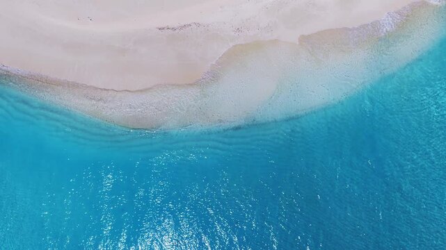 Aerial top down sweep over Dhigurah Island, Maldives shows a narrow crescent sandbar meeting a lagoon, reef textures, surf lines, sun glints, and gentle tidal motion.