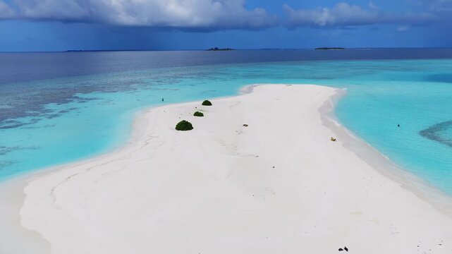 Aerial view of Dhigurah, Maldives, with white sandbar curving into a turquoise lagoon, deeper ocean, low atolls, tiny figures wading, gentle waves, and rain band on horizon