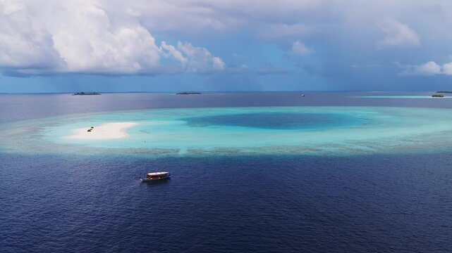 Aerial view shows Dhigurah island atoll, a white sandbank with reefs, a drifting dhoni, tiny visitors and three vegetation clumps, under cumulus and a distant rain shaft.