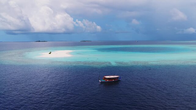 Aerial view of Dhigurah island, Maldives, deep navy ocean to turquoise lagoon, white sandbank, dhoni floats, tiny figures in shallows, cumulus clouds, soft daylight
