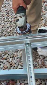 Close up video of worker hands using electric angle grinder with flap disc and smooth edges of galvanized square steel pipe at outdoor construction site. Metal fabrication concept.
