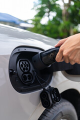 Fototapeta premium Side view of an Asian woman's hand refuel an electric vehicle with a charger plug. Concept of alternative power infrastructure green tech and sustainability. Vertical Shot